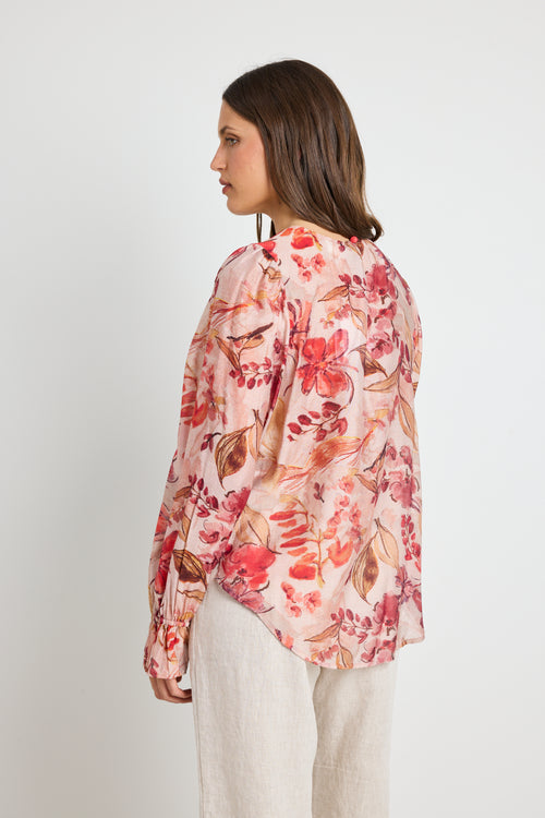 Woman wearing a blush floral top with flowy sleeves, paired with natural linen pants for an elegant and relaxed look.