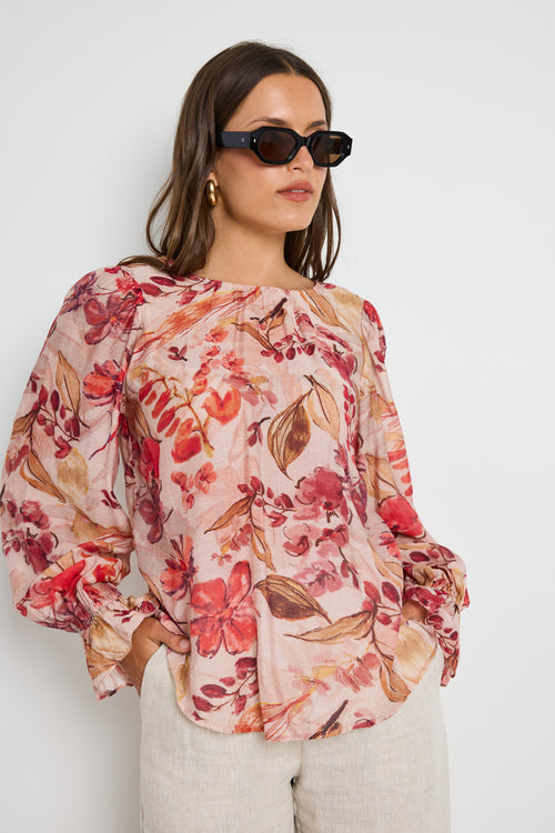 Woman wearing a blush floral top with flowy sleeves, paired with natural linen pants for an elegant and relaxed look.