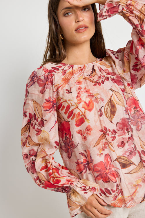 Woman wearing a blush floral top with flowy sleeves, paired with natural linen pants for an elegant and relaxed look.