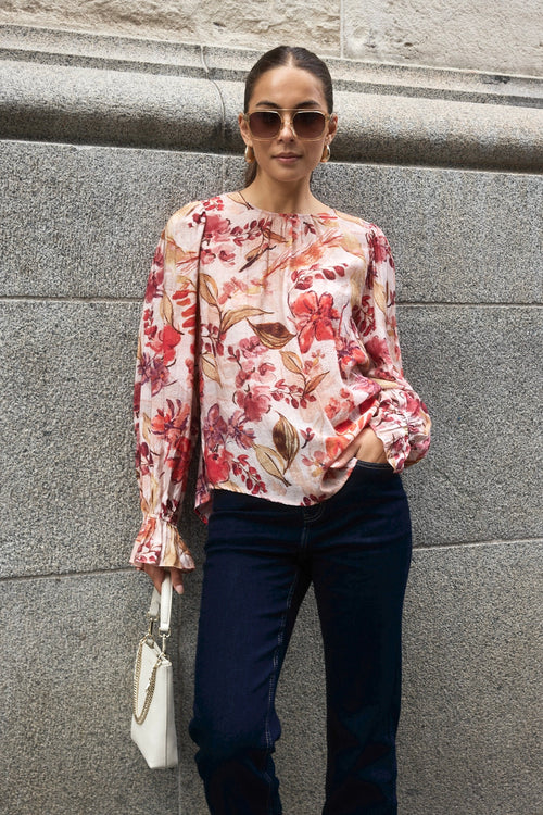  Woman wearing a blush floral top with flowy sleeves, paired with natural linen pants for an elegant and relaxed look.