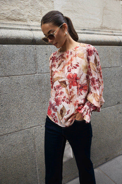 Woman wearing a blush floral top with flowy sleeves, paired with natural linen pants for an elegant and relaxed look.