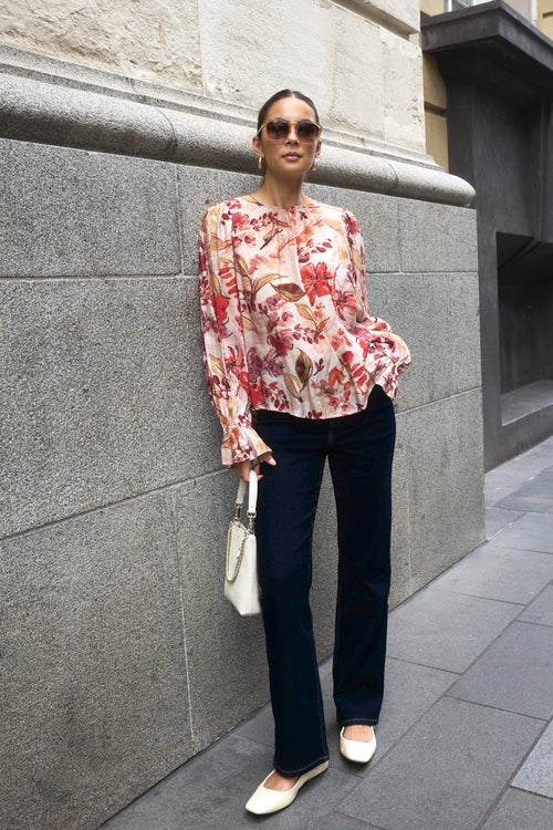 Woman wearing a blush floral top with flowy sleeves, paired with natural linen pants for an elegant and relaxed look.