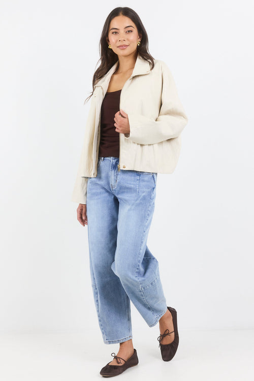 Woman wearing a cream jacket, brown top, and light blue jeans on a white background