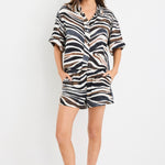 Woman wearing mid-rise chocolate zebra print shorts with an elastic waistband, styled casually with a black top and black sandals.