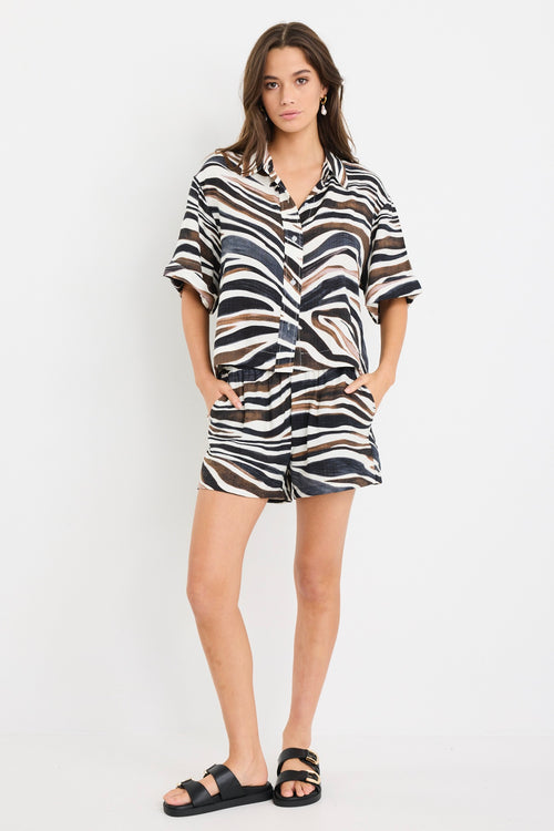 Woman wearing a relaxed-fit short sleeve zebra print shirt in chocolate, black, and white tones, styled with high-rise blue jeans.