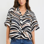 Woman wearing a relaxed-fit short sleeve zebra print shirt in chocolate, black, and white tones, styled with high-rise blue jeans.