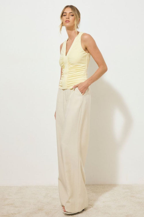 Lemon yellow sleeveless tank top with ruched bodice and centre band detail, styled with light beige wide-leg pants, worn by a model standing against a neutral background.