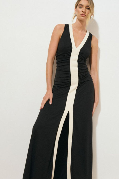 Black sleeveless midi dress with a low V-neckline, contrast cream band detail down the centre front, ruched bodice, and front hem split, worn by a model standing against a white background.