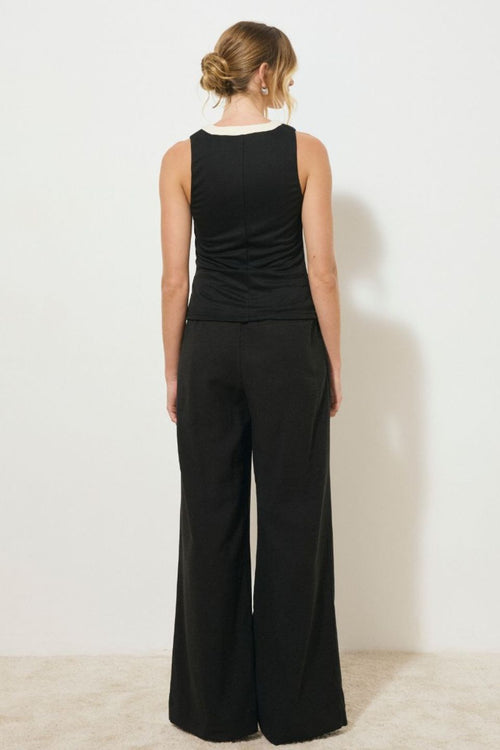 Black sleeveless tank top with contrast cream band detail down the centre front and neckline, featuring a ruched bodice and low V-neckline, worn by a model sitting against a neutral background.