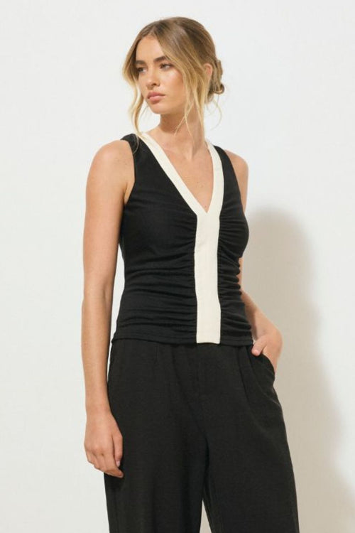 Black sleeveless tank top with contrast cream band detail down the centre front and neckline, featuring a ruched bodice and low V-neckline, worn by a model sitting against a neutral background.