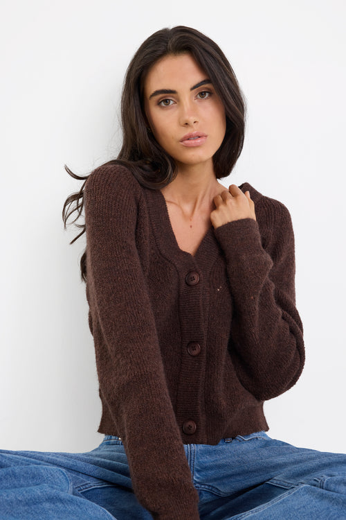 Woman wearing a brown cardigan and blue jeans against a white background