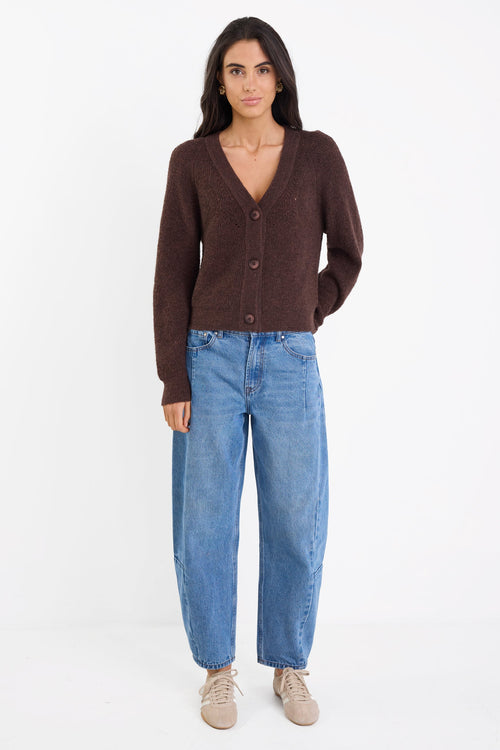 Woman wearing a brown cardigan and blue jeans on a white background