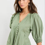 Woman wearing a green blouse with puffed sleeves against a white background