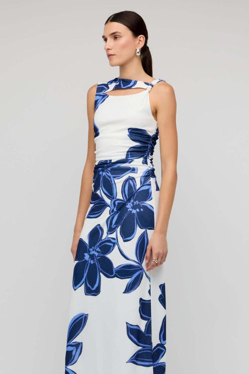 Woman wearing a sleeveless white midi dress with large blue floral print, featuring a side cutout detail and slim fit through the waist.