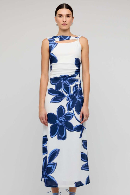 Woman wearing a sleeveless white midi dress with large blue floral print, featuring a side cutout detail and slim fit through the waist.