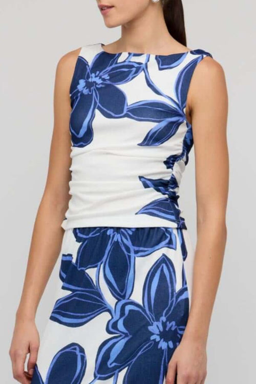 Woman wearing a white sleeveless mesh top with bold blue floral print, styled with blue denim jeans for a casual yet polished look.