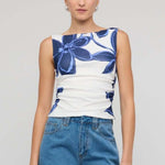 Woman wearing a white sleeveless mesh top with bold blue floral print, styled with blue denim jeans for a casual yet polished look.