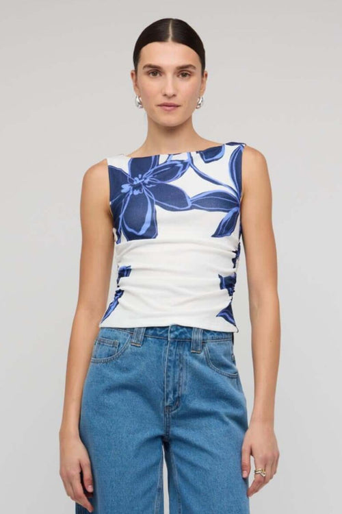 Woman wearing a white sleeveless mesh top with bold blue floral print, styled with blue denim jeans for a casual yet polished look.