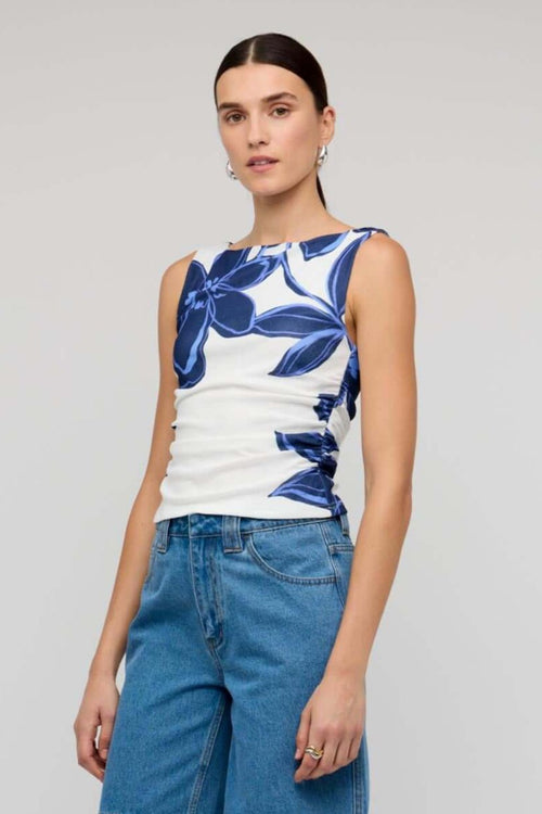 Woman wearing a white sleeveless mesh top with bold blue floral print, styled with blue denim jeans for a casual yet polished look.