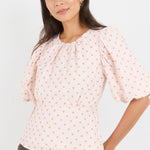Woman wearing a light pink blouse with puff sleeves against a white background
