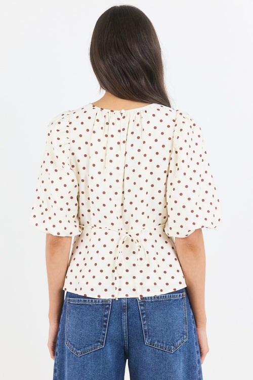 Person wearing a white blouse with red patterns and blue jeans on a light gray background