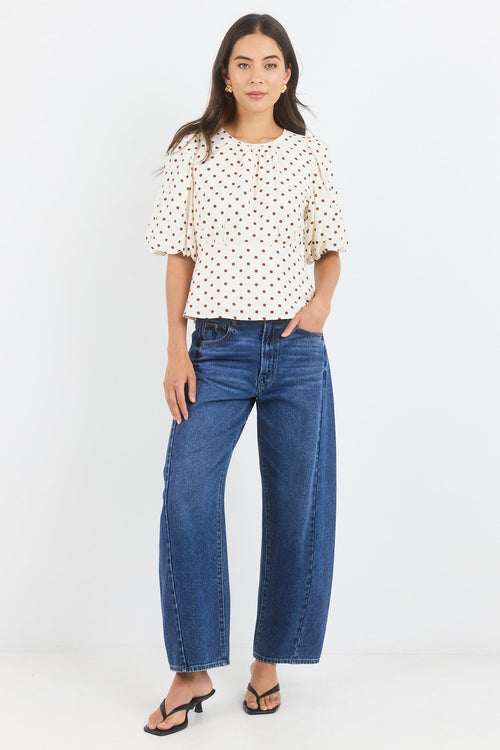 Woman wearing a polka dot blouse and blue jeans on a white background