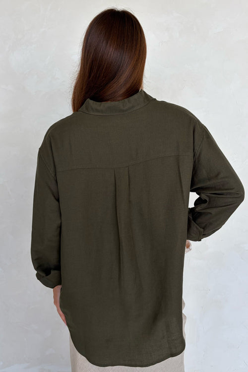 Person wearing an olive green shirt against a white wall
