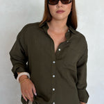 Woman wearing an olive green button-up shirt and sunglasses against a white background