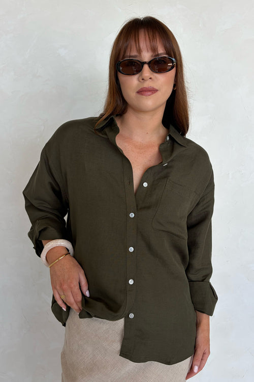 Woman wearing an olive green button-up shirt and sunglasses against a white background