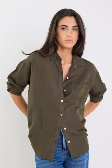 Woman wearing an olive green shirt and blue jeans against a white background
