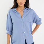 Woman wearing a light blue button-up shirt and dark blue jeans against a white background