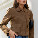 Woman wearing a brown jacket and blue jeans against a white wall.