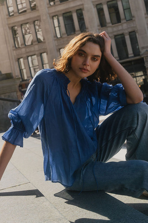 Woman in a blue outfit sitting on a city street with a large building in the background