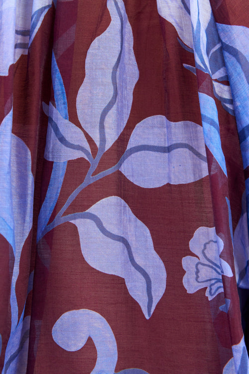 A close-up of a sheer fabric with a botanical leaf pattern in dusty burgundy red, light blue, and lavender.