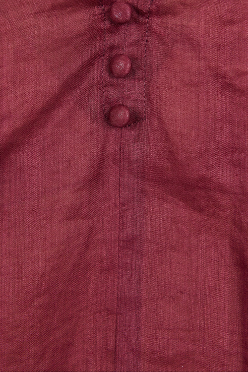 Close-up of a burgundy or deep wine-colored top with a V-neckline and three matching fabric buttons down the center front.