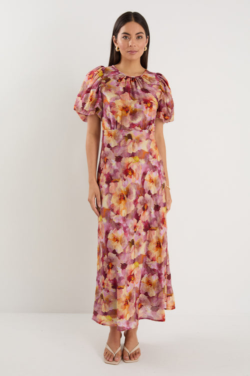 Woman wearing a pink and multi-tone floral midi dress with puff short sleeves, bias cut, and lined finish.
