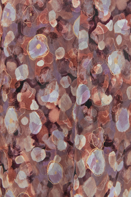 A woman wearing a floral midi dress in shades of lilac, blush, and soft pink, with puffed short sleeves and a relaxed fit.