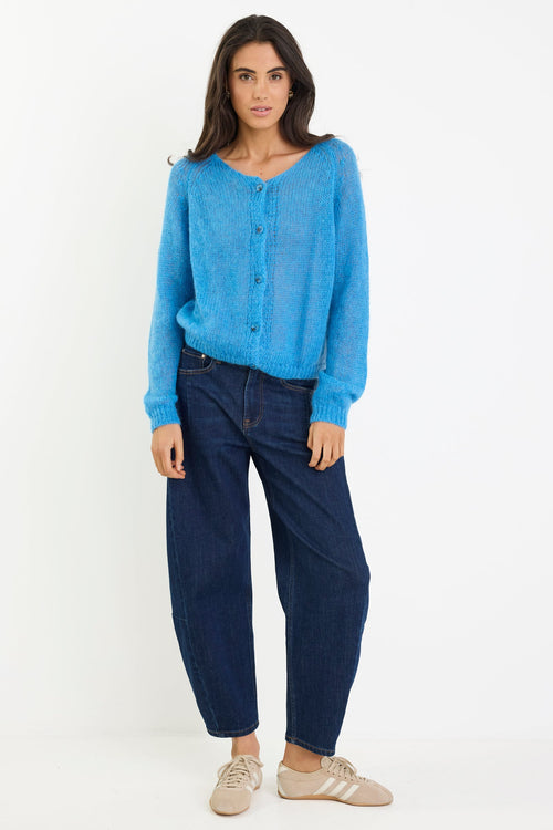 Woman wearing a blue sweater and dark jeans on a white background