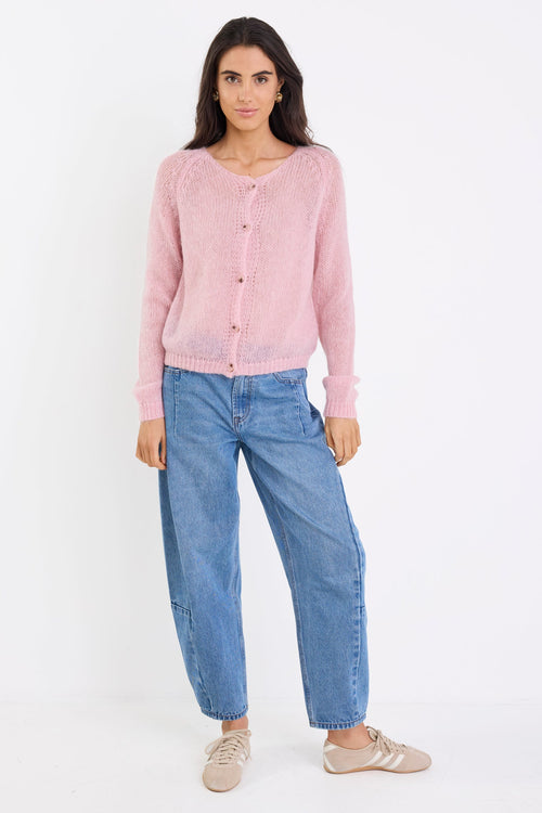 Woman wearing a pink cardigan and blue jeans on a white background