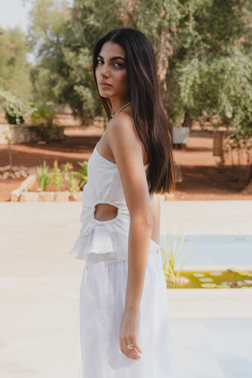 model is in a white top and white pants by a pool