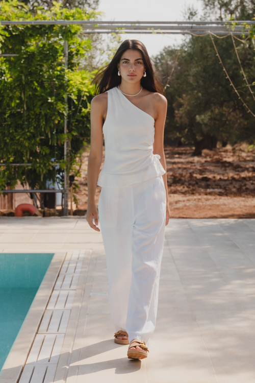 model is in a white top and white pants by a pool