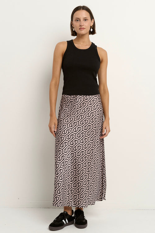 Woman wearing a blush and black geometric print satin midi skirt with a black tank and sneakers.







