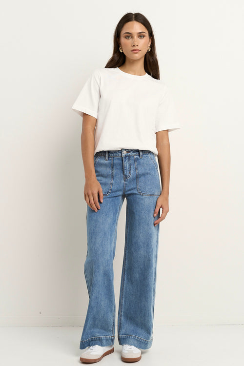 Woman wears a white tee with mid-rise, wide-leg blue jeans featuring front patch pockets and a relaxed silhouette.