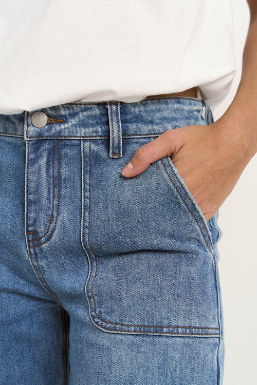 Woman wears a white tee with mid-rise, wide-leg blue jeans featuring front patch pockets and a relaxed silhouette.