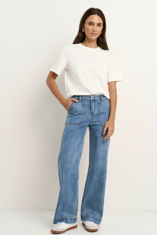 Woman wears a white tee with mid-rise, wide-leg blue jeans featuring front patch pockets and a relaxed silhouette.