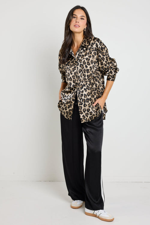 Woman wearing a leopard print satin shirt with a relaxed fit, paired with black satin pants for an effortlessly chic look.