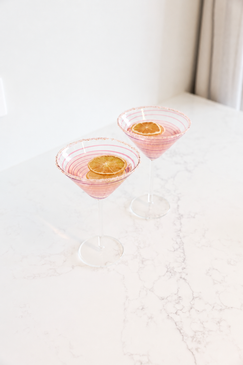 Fiesta Pink Swirl Stripe Martini Glass in clear glass with delicate pink spiral detailing, styled on a light marble surface.