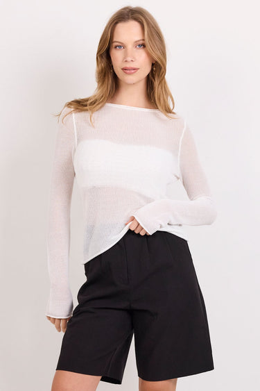 A woman modeling a white sheer long-sleeve top and black shorts against a plain white studio background.