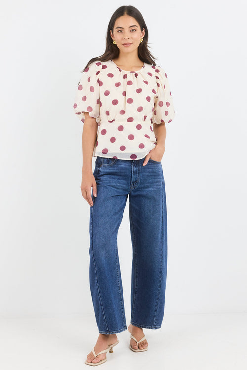 Woman wearing a polka dot blouse and blue jeans on a white background