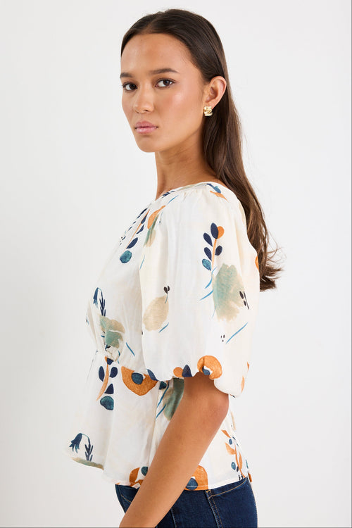 Woman wearing a cream and patterned top with blue jeans